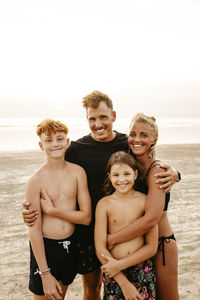 Portrait of smiling family standing at beach during sunset