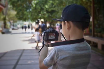 Rear view of boy photographing while standing on footpath in city