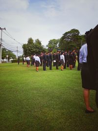 Rear view of people standing on field against sky
