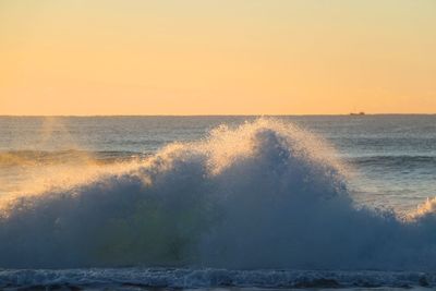 Waves flowing in sea against sky during sunset