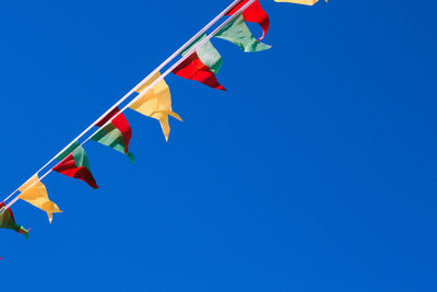 Low angle view of triangular multicolored flags against clear blue sky