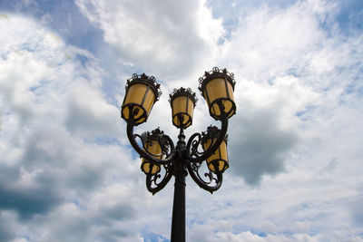 Low angle view of electric lamps against cloudy sky