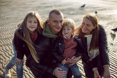 Family in a leather jacket stands along the beach with their dog in autumn