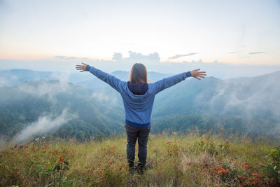 Rear view of woman with arms outstretched standing on mountain against sky