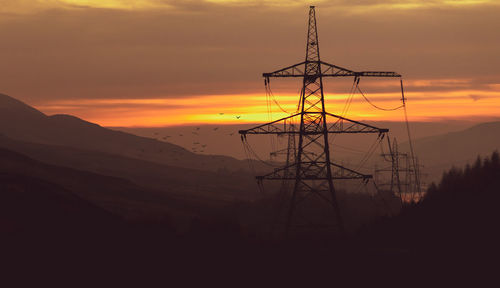 Silhouette electricity pylons on land against sky during sunset