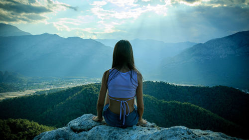 Rear view of woman sitting on mountain against sky