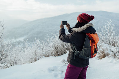 Woman photographing on snowcapped mountain