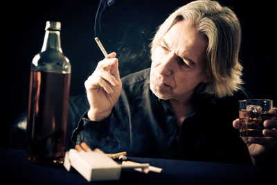 Close-up of man holding cigarette against black background