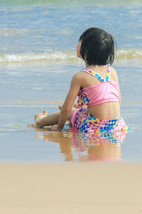 Rear view of girl sitting at beach against sea