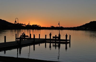 Silhouette wooden posts in lake against orange sky