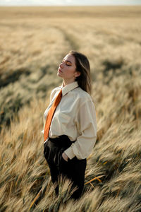 Side view of young mindful female in formal wear with tie and closed eyes among spikes in countryside