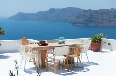 Furniture composed by a table and some chairs on a white terrace of a house in santorini greece where you can enjoy meal while seeing a romantic seascape to the blue aegean sea. horizontal ph