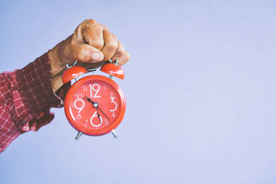 Cropped hand of man holding alarm clock against wall