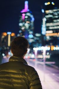 Rear view of man standing by illuminated buildings in city at night