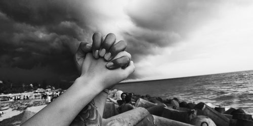Cropped image of couple holding hands at beach against cloudy sky