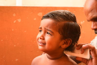 Close-up of barber cutting boy hair against wall