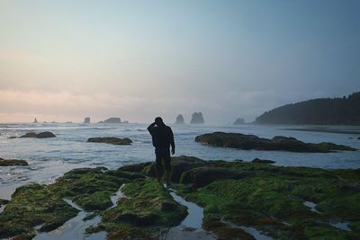 Man standing at rocky sea shore against sky