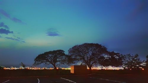 Silhouette trees on landscape against blue sky