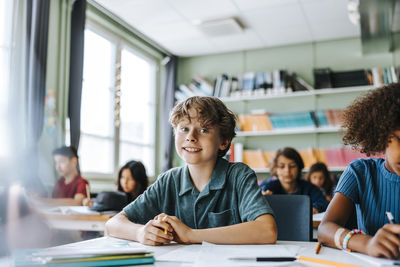 Portrait of cute boy sitting in classroom with classmates at elementary school