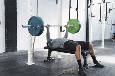 Sportsman exercising with barbell lying on bench in gym