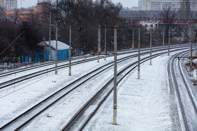 Snow-covered railroad tracks in a turn and a blue gatehouse in a thicket of bushes.