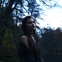 Young woman looking away against trees