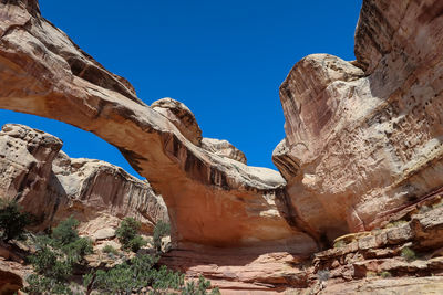 Low angle view of rock formation and arch against clear blue sky