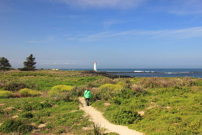 Rear view of woman walking by sea against sky