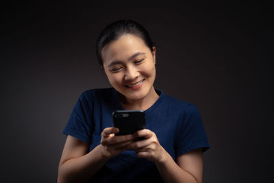 Portrait of smiling man holding mobile phone against black background