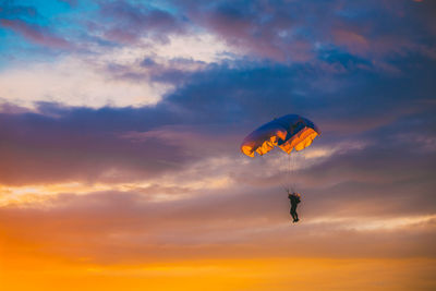 Low angle view of silhouette person paragliding against orange sky