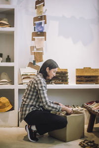 Full length side view of saleswoman crouching by box at boutique