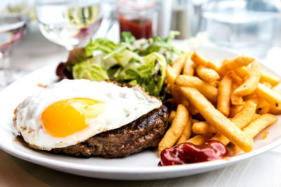 Close-up of fried egg with french fries and meat served on table