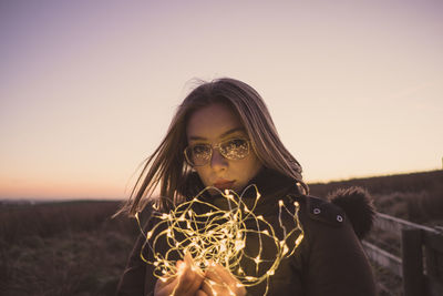 Portrait of beautiful woman in field against sky during sunset