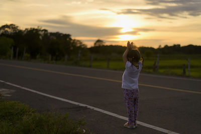 Rear view of woman walking on road against sky during sunset