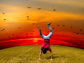 Full length rear view of man doing handstand on grass during sunset