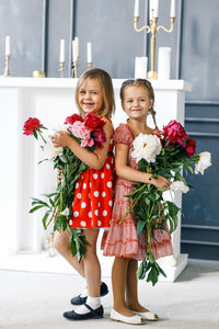 Portrait of smiling siblings with flowers standing at home