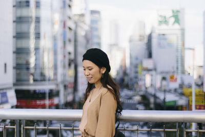 Young woman looking away while standing on railing in city