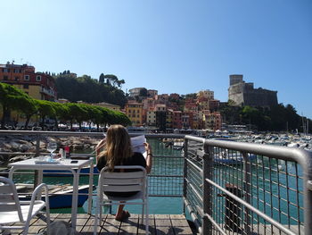 Rear view of woman sitting at harbor in city