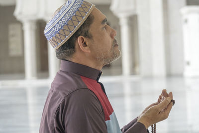 Side view of mature man praying while kneeling at mosque