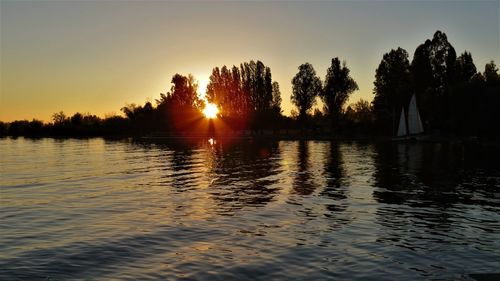 Silhouette trees by lake against sky during sunset