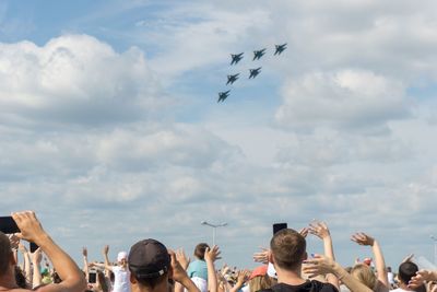 Low angle view of people watching airshow against sky