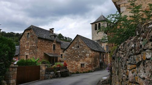 Narrow road along houses against cloudy sky