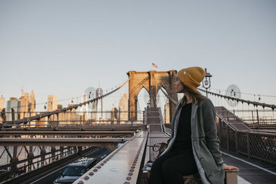 Usa, new york, new york city, female tourist sitting on brooklyn bridge in the morning light
