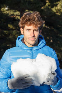 Portrait of young man holding snow standing outdoors