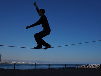 Man on tightrope at beach against clear blue sky