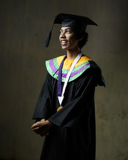 Smiling man in graduation gown standing against wall