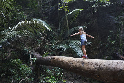 Girl balancing on fallen tree trunk in forest