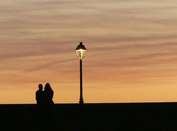 Silhouette people on street light against orange sky