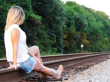 Rear view of woman sitting on railroad track against trees