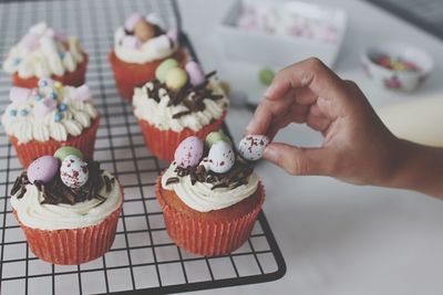 Close-up of hand decorating cupcake on cooling rack